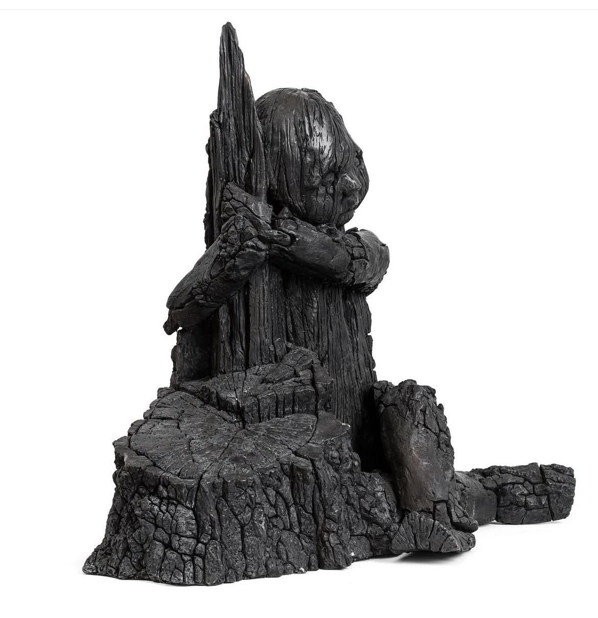 Skulptur af forkullet træ forestillende en sammenkrøbet figur, der omfavner en stub. Værket har en rå, sort tekstur og fremstår ladet med sorg og stilhed. Titel: A Grief…. Skabt i 2022, 70 × 70 × 48 cm, oplag 3 af 7.